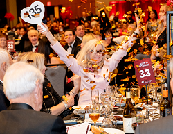 Woman holding up bidder paddle as confetti falls on her table